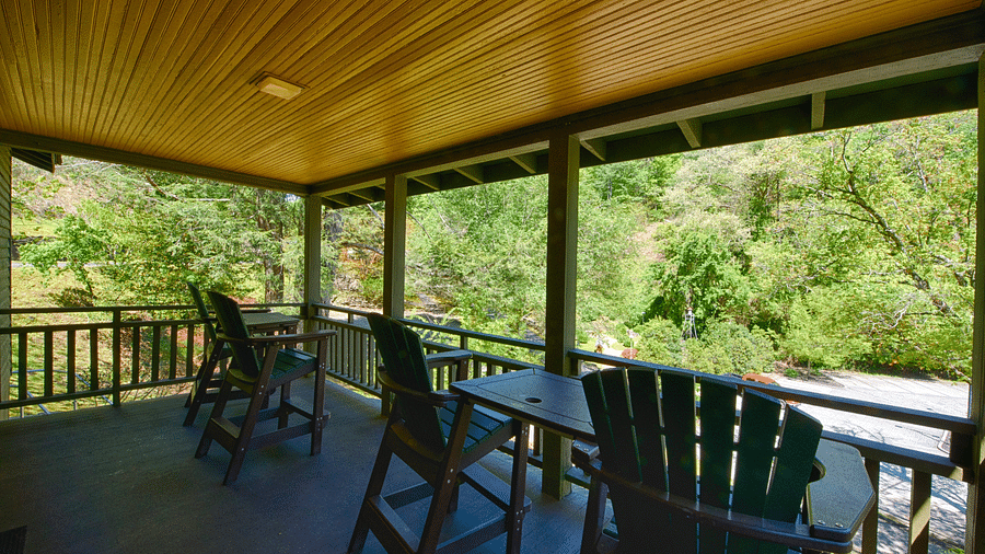 corner view of the porch with four chairs kept facing towards the serene green forest during the day timefull view image of a bedroom with wooden interiors featuring two beds - Historic Tapoco Lodge