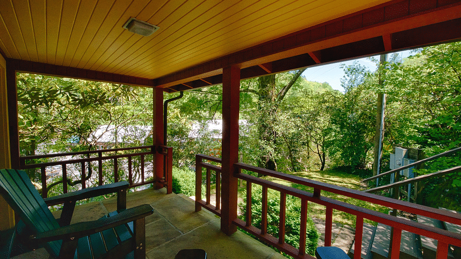 a beautiful wooden porch with chairs kept on it facing towards the green forests - Historic Tapoco Lodge