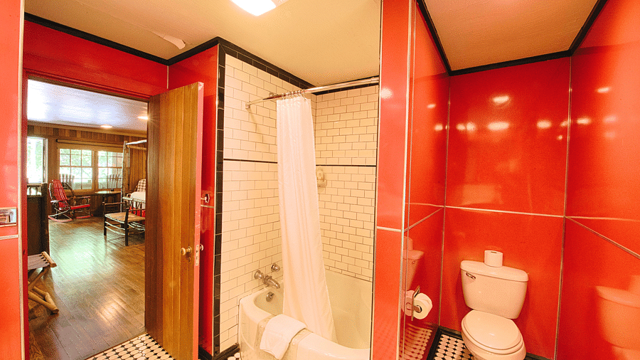 a bathroom with bright red tiles on the wall featuring a commode and a bathtub along with a door opening inside the room - Historic Tapoco Lodge
