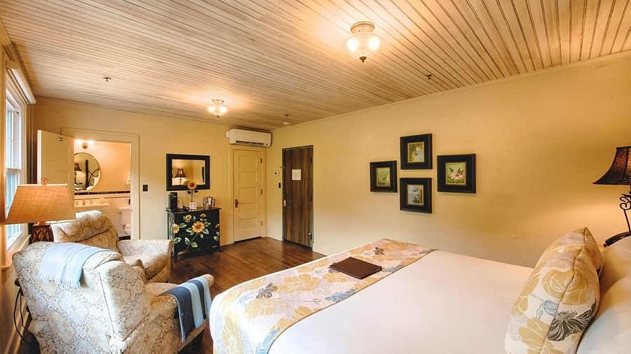 a cozy bedroom with minimalist and sleek interiors featuring a double bed and the back of a cushioned armchair - Historic Tapoco Lodge