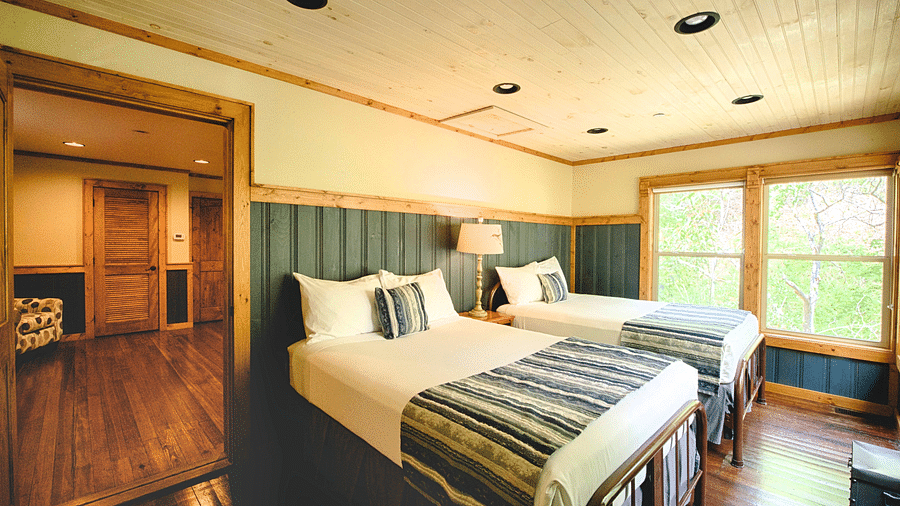 a room with ample natural light featuring two single beds with an open door frame besides them - Historic Tapoco Lodge