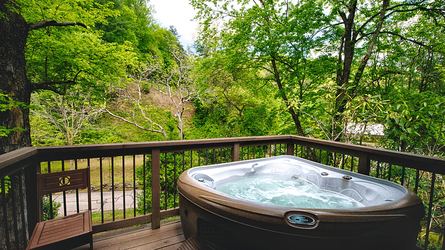 a wooden porch with hand railings along with a Jacuzzi tub overlooking the beautiful surrounding forest views - Historic Tapoco Lodge