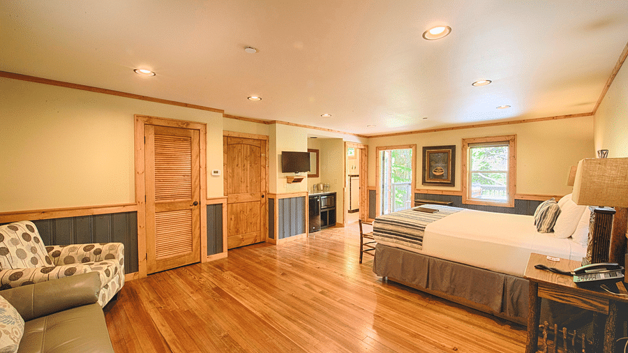 a bedroom with a double bed and a common seating area in the corner with two wooden doors right in front of it - Historic Tapoco Lodge