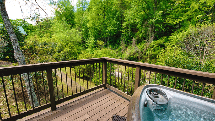 a wide angle shot of a wooden porch with a Jacuzzi tub and lush green views -Historic Tapoco Lodge