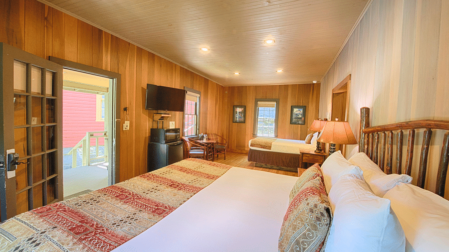 a room with wooden walls featuring two double beds with plush pillows and cushions along with a wall mounted television - Historic Tapoco Lodge