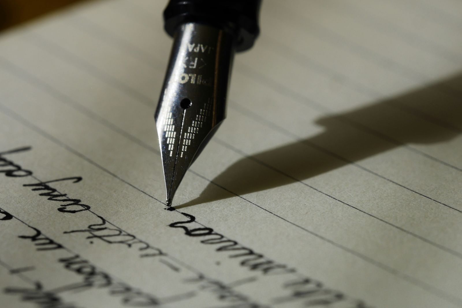  A close-up shot of a fountain pen nib touching a piece of lined paper with handwritten cursive text.
