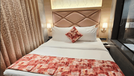 A room at Hotel Mumbai House, Digha Airoli, with a large bed, pillow, bedspreads, and a window covered with curtains.