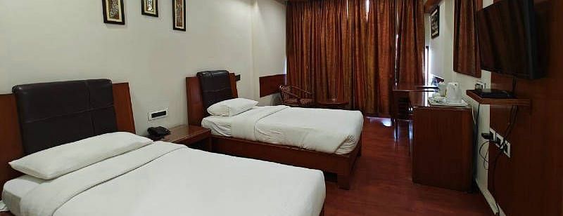 A bedroom with two single beds and dark wooden flooring along with a wall mounted television - Hotel Gold, Panipat
