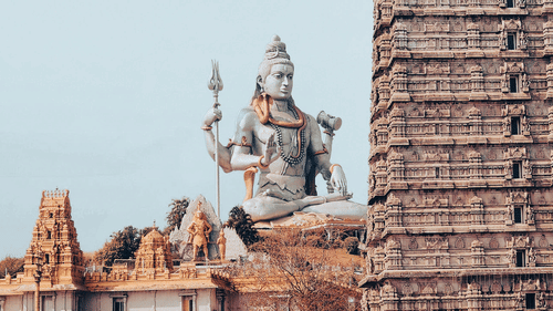 View of a statue of Lord Shiva with a temple gopuram in the foreground