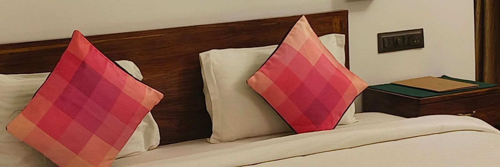 Front view of a double bed with two pink pillows kept on it and hexagonal frames hanging on the wall in 101 non-ac room at Ananda Holiday Home, Wayanad 1