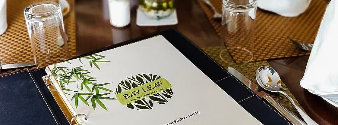 A restaurant table is set with a menu, glassware, cutlery, and napkins. - Bamboo Saa, Udaipur