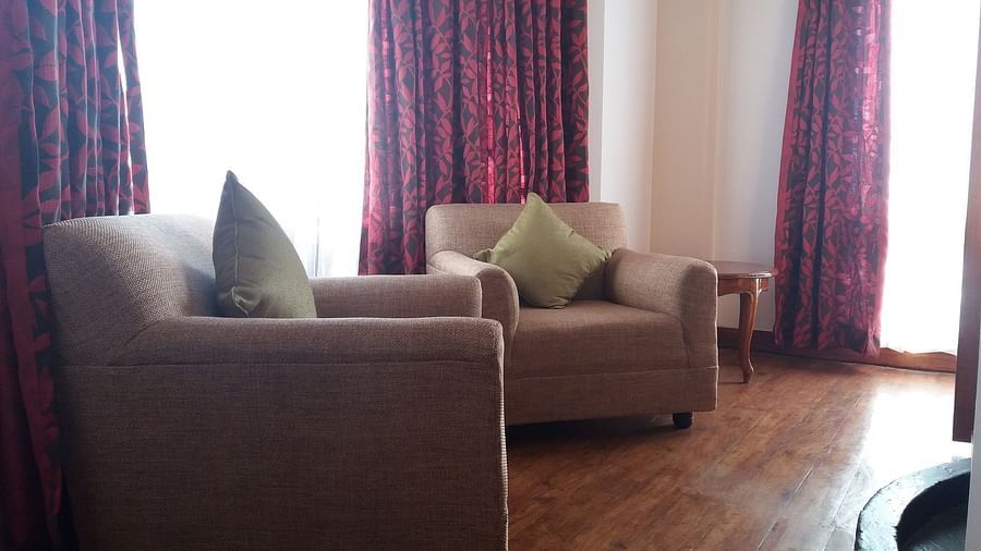 The separate sitting area in the Executive Suite of Cedar Inn in Darjeeling has two cushioned sofas, curtained glass windows and wooden flooring.