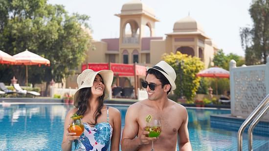 A couple holding drinks in their hands posing in the swimming pool - Heritage Village Resorts & Spa, Manesar