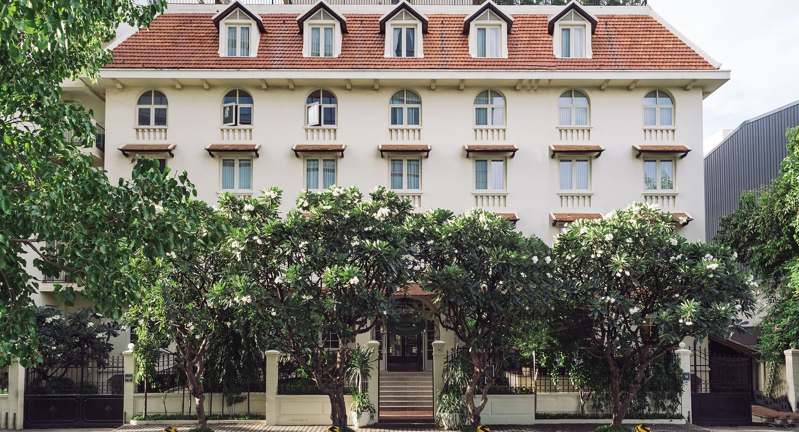 A multi-storey building with a distinctive roof line, framed by foliage | Central Mansions, Phnom Penh