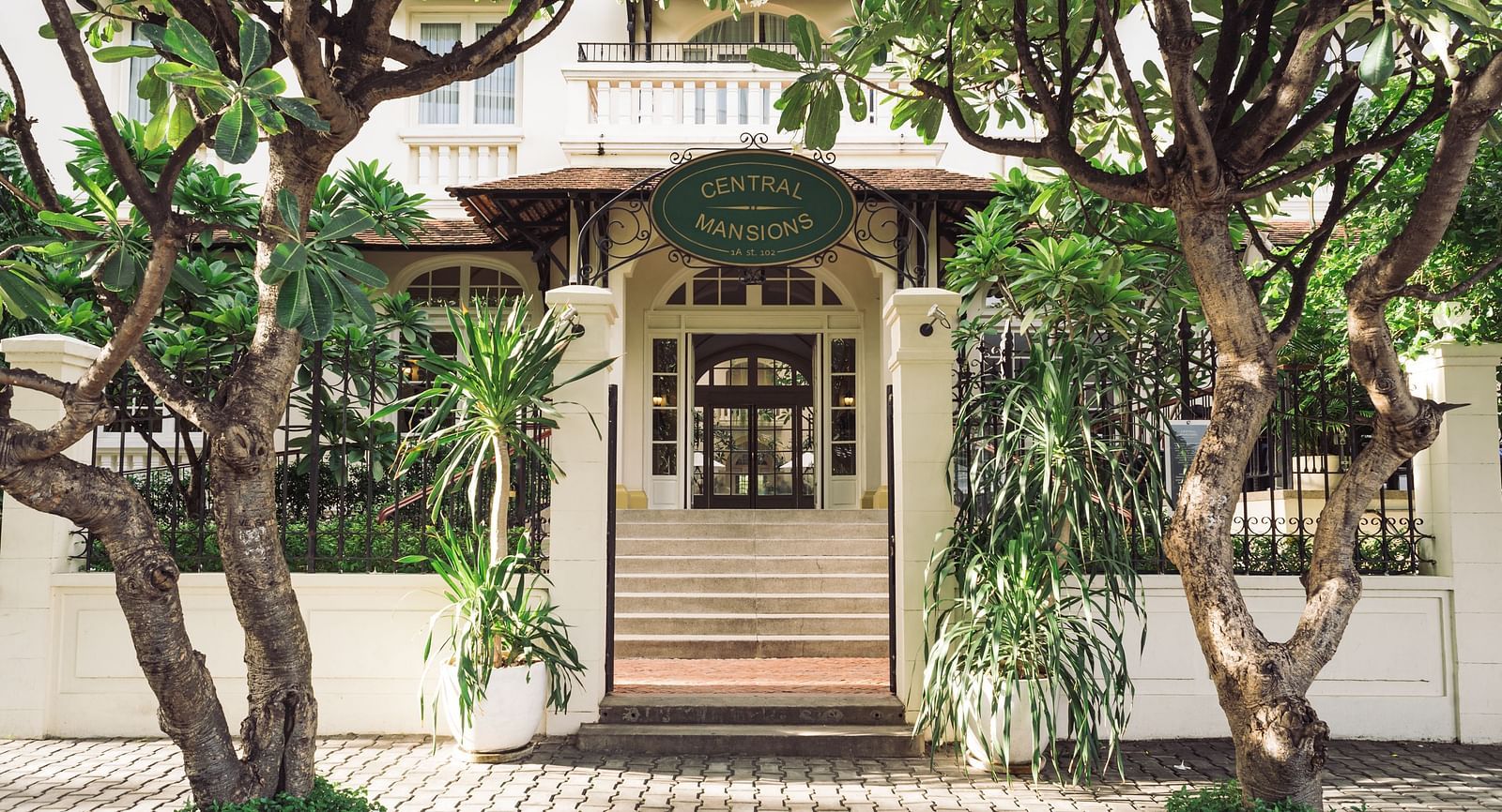 A close-up of an entrance with a staircase, surrounded by trees | Central Mansions, Phnom Penh