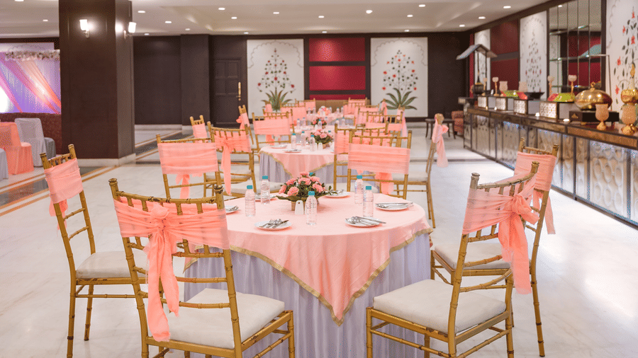 Round tables with gold chairs arranged in the Raj Mahal banquet hall in Nathdwara at Shri Vallabh Vilas Lords Plaza.