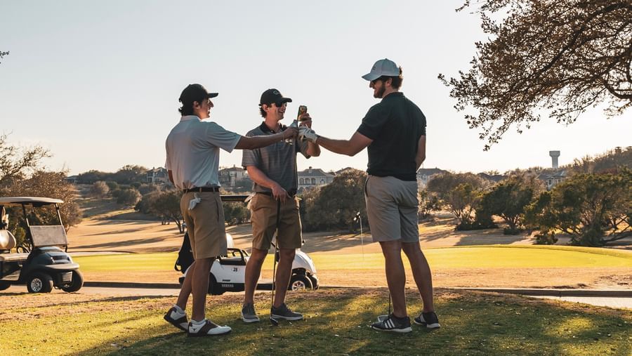 Three golfers toasting with drinks on a sunny golf course, celebrating a successful game.