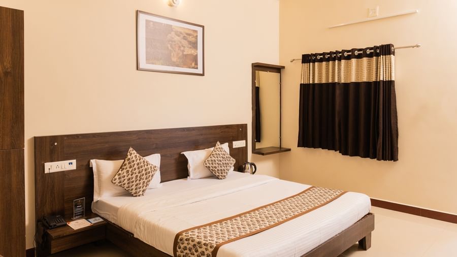 A room with a double bed, a mirror, brown and beige curtains, and a wall art at Daksh Resort & Amusement Park, Sasan Gir.