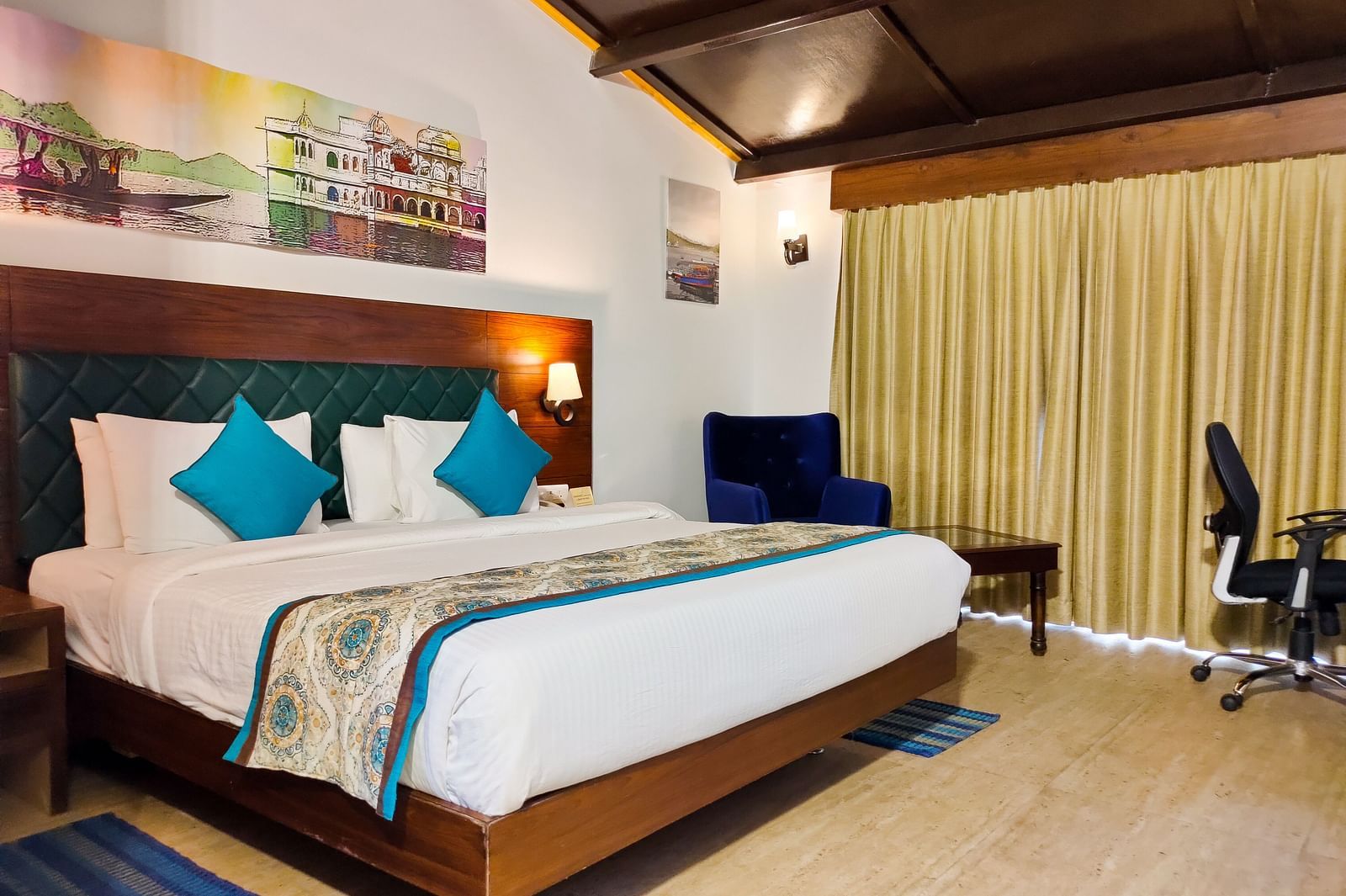 A hotel room featuring a large bed with pillows, a desk, and a armchair. - Bamboo Saa Resort & Spa, Udaipur