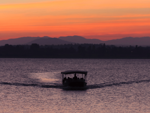 A boat cruising through a river during sunset with the hills visible in the background.