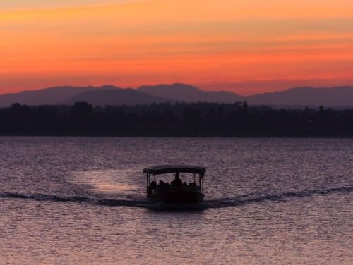 A boat cruising through a river during sunset with the hills visible in the background.