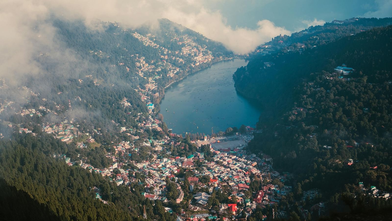 A scenic view of the city of Nainital surrounded by mountains with a river passing by.