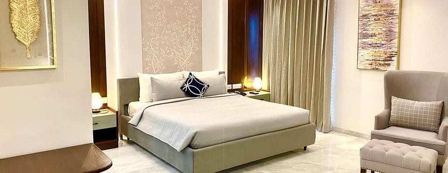 An image of a room with a well made king-sized bed, elegant decor, marble flooring, warm lighting, and a cosy chair - The Manohar, Hyderabad
