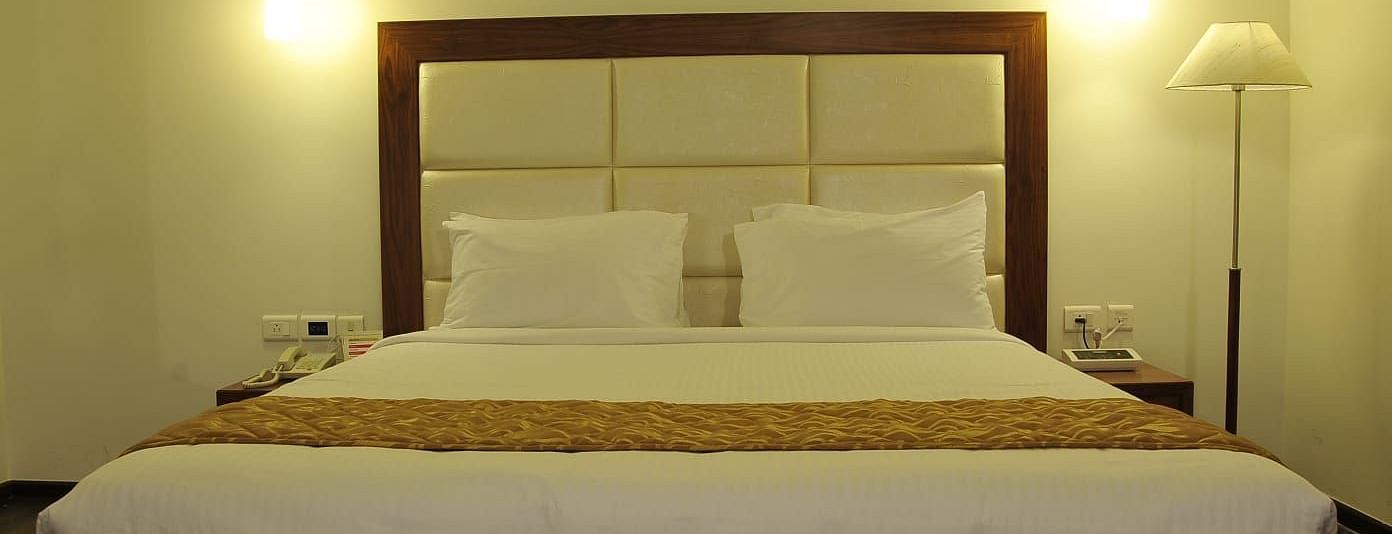 Close up of Suite at Dhanalakshmi Srinivasan Hotels, Perambalur featuring kind bed, furniture, and warm lighting. 