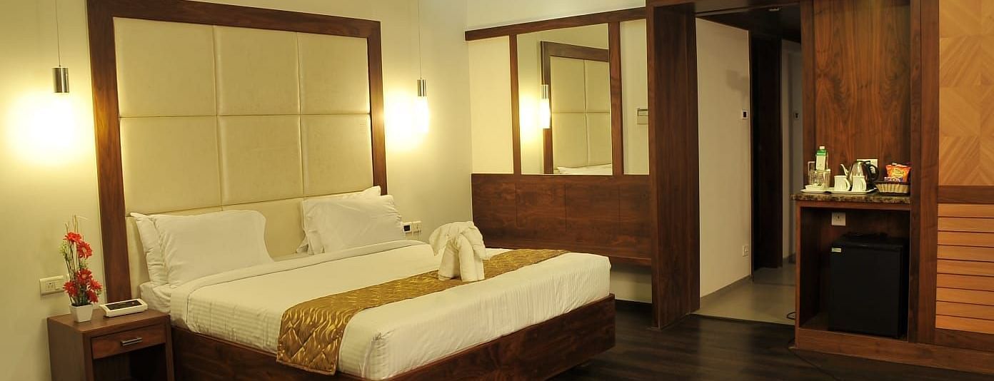A Executive Suite at Dhanalakshmi Srinivasan Hotels, Perambalur featuring a bed with white linens, dark wood flooring, and a mini-fridge.