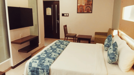 A hotel room layout showing a king size bed, a wall-mounted television, a wooden chair with a small side table, and an entry door at Hotel Mumbai House, Thane.