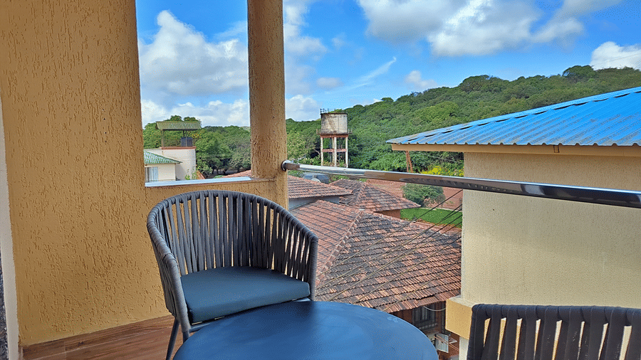 Balcony with chairs and a round table overlooking green hills and surrounding buildings