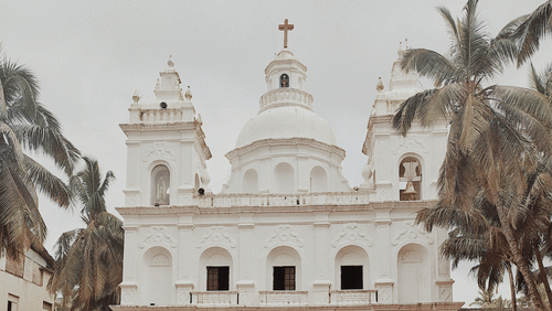 The exterior view of a church, with coconut trees in the background.