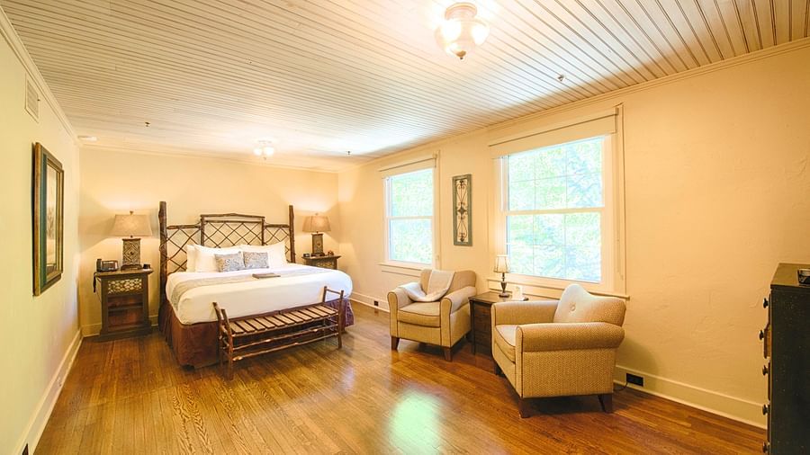 corner view image of a spacious bedroom featuring a common seating area along with a comfortable double bed - Historic Tapoco Lodge