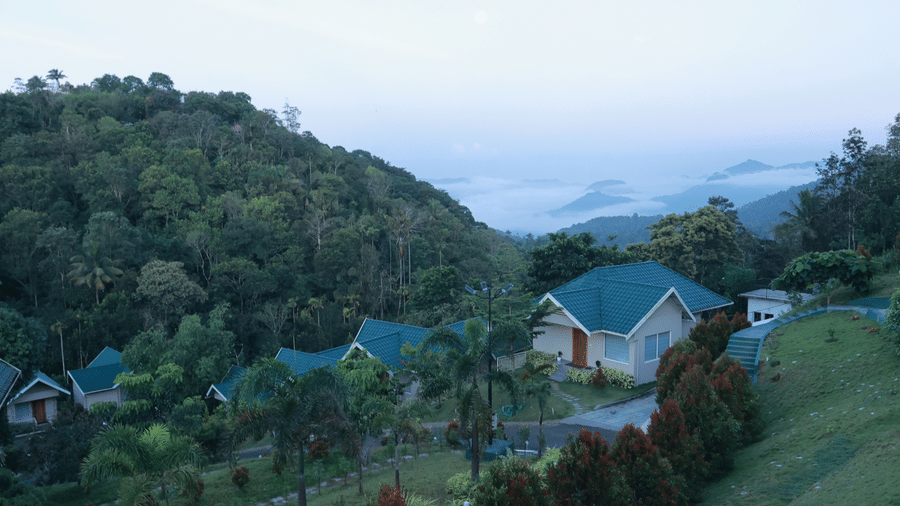 A villa nestled amidst lush green gardens and well-manicured trees with cloud covered valleys at a far away distance from Aveda Mountains and Mist Resort and Spa, Munnar.
