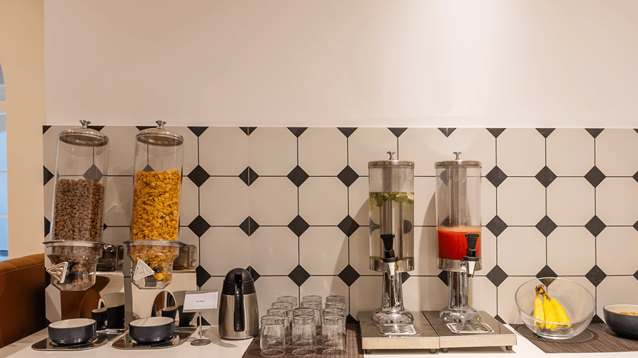Breakfast counter with cereal dispensers, a kettle, glasses, juice dispensers and bananas at M-Salt at Monday Hotels & Suites Madhapur, Hyderabad.