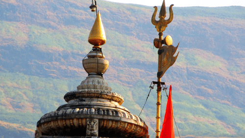 A temple dome with a golden finial and a trident symbol with hills visible in the background.