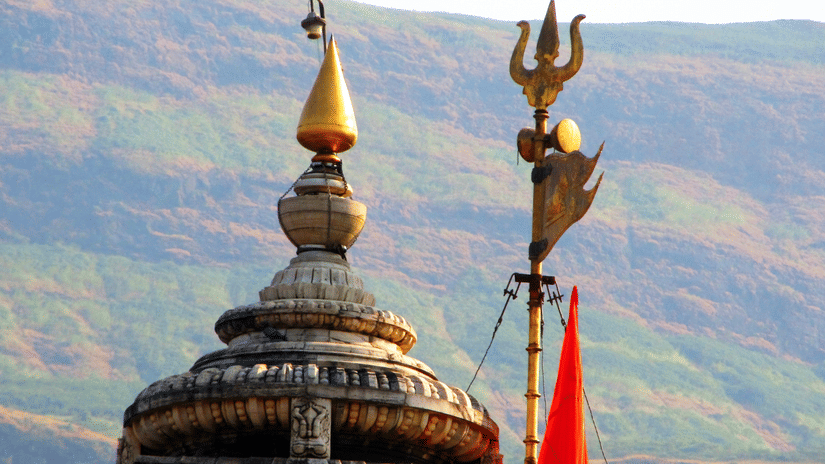 A temple dome with a golden finial and a trident symbol with hills visible in the background.
