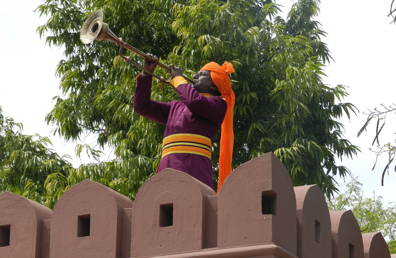A man in traditional attire playing an instrument atop a fortified wall  - Khas Bagh, Jaipur.