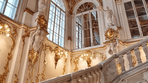 An interior with arches, chandeliers, carved railings, and decorative windows.