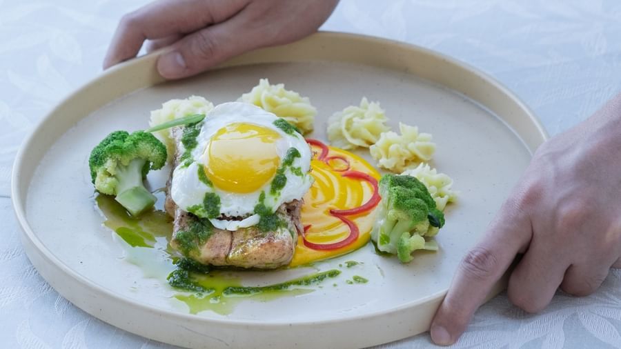 A person keeping a plate of Grilled Fish with Poached Egg on a table | Mango Hill, Pondicherry