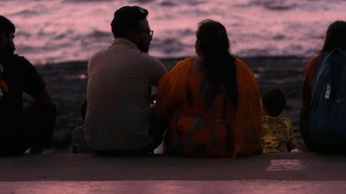 A couple sitting on the steps in front of a beach in the evening time