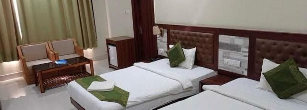 A twin room with white linen and green cushions, ideal for a comfortable and relaxed visit - Pemaling Lords Eco Inn Guwahati