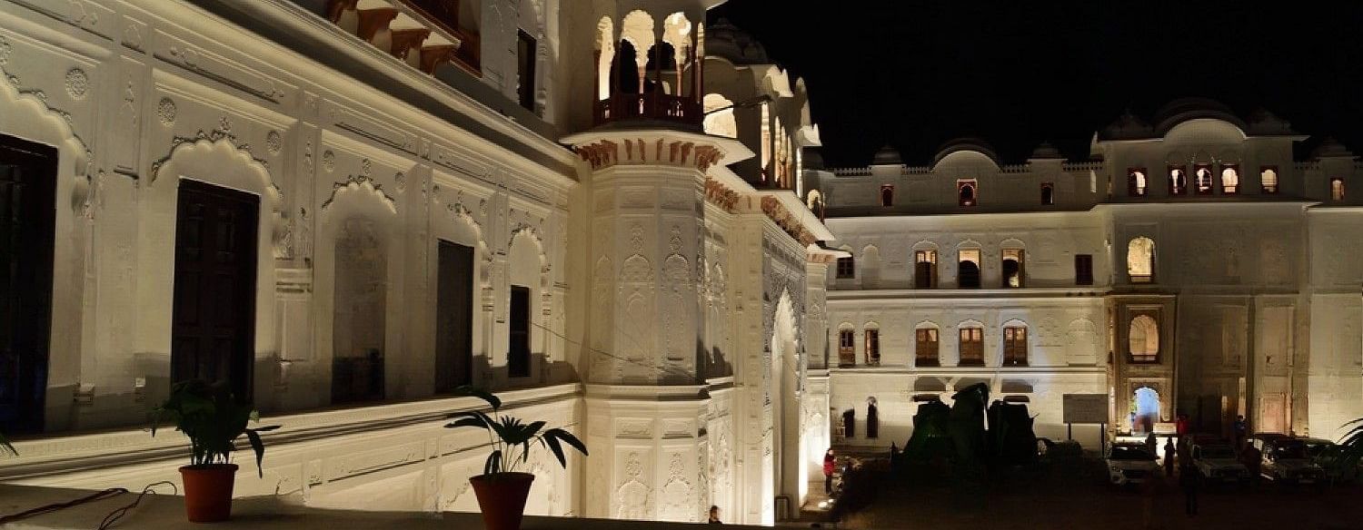 A large, illuminated palace with multiple towers and balconies, surrounded by a courtyard.