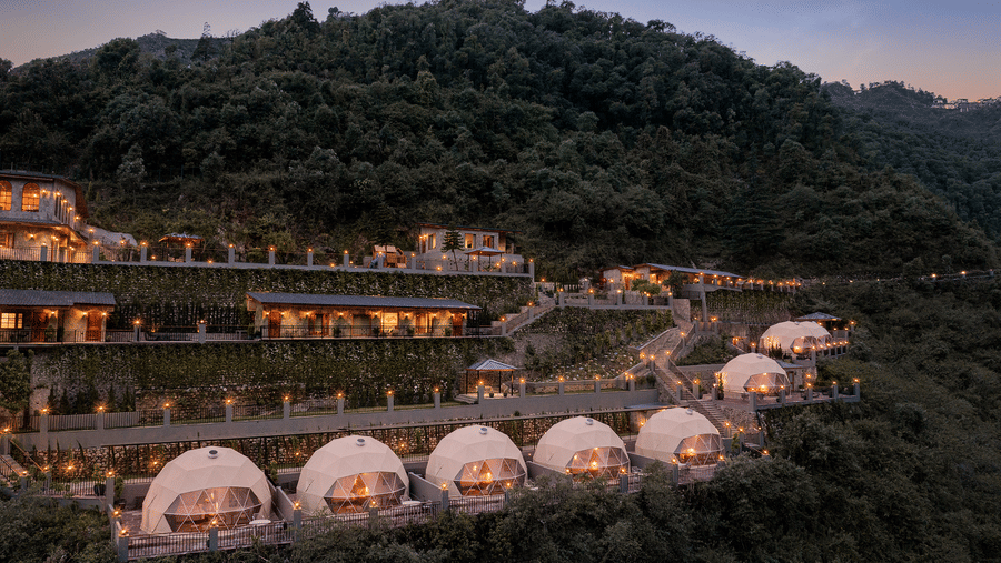 Scenic dusk view of a luxury resort terraced on a green mountain slope with dome accommodations.
