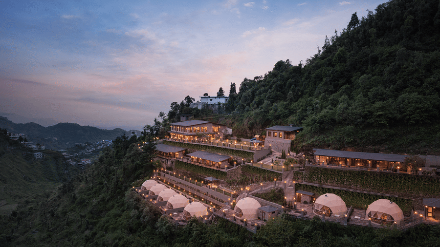 Scenic dusk view of a luxury resort terraced on a green mountain slope with dome accommodations.