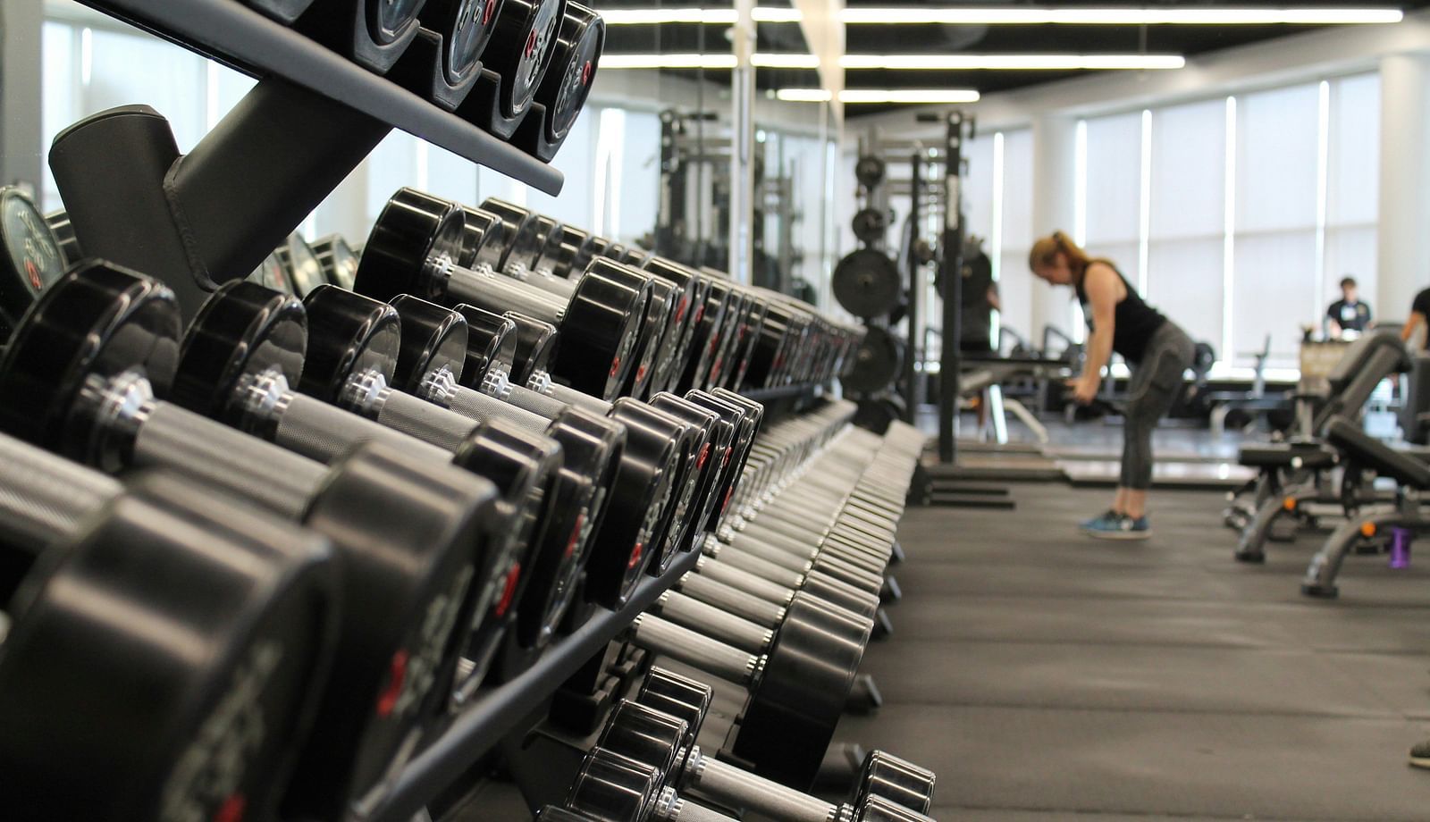 A close up shot of dumbbells in a rack with a person in the background working out