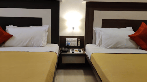 Vertical view of twin beds made with mustard yellow linens separated by a small white bedside table.