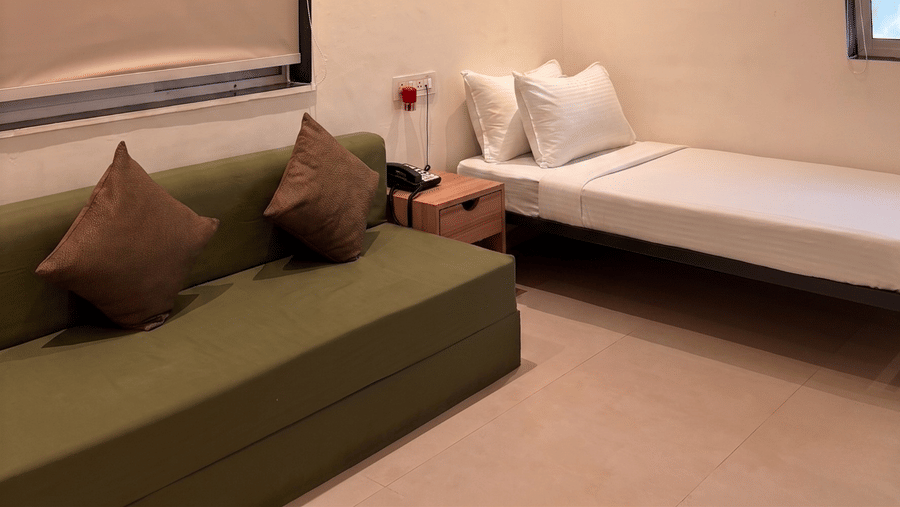 A room interior at Oceanature Resort, Alibaug showing a green sofa with brown cushions, a single bed, and a wall frame.