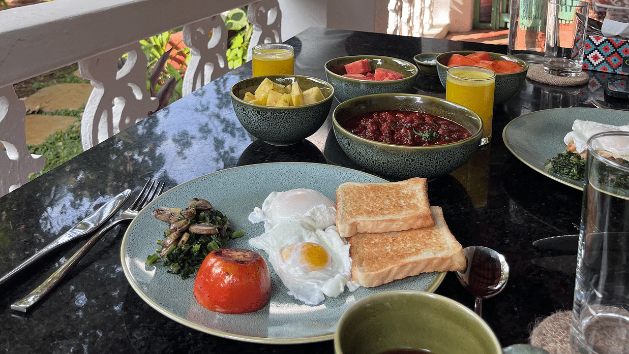 An image of a breakfast table where several dishes are placed like omelette, bread, curries, bowl of fruits, a glass of cold drink and lot more at Lamrin Ucassaim Hotel, Goa