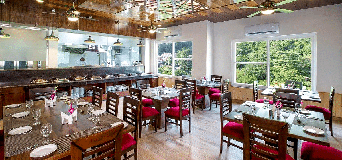 Full view shot of the restaurant at Regenta Inn DLS with neatly arranged dining tables with ample of natural lighting inside.